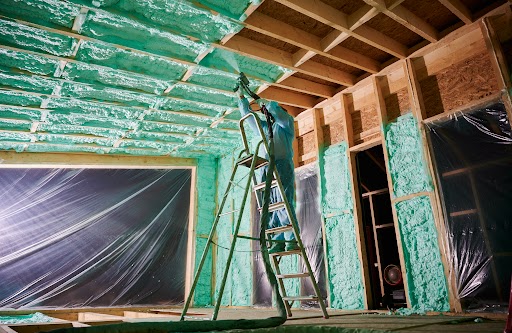 Male builder insulating wooden frame house. Man worker spraying polyurethane foam inside of future cottage, standing on ladder, using plural component gun. Construction and insulation concept.